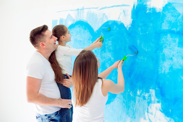 Mother, father and little daughter painting the wall in their new home.