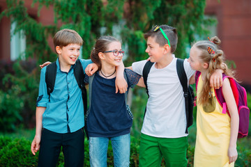 Children's friendship. Four little school students, two boys and two girls, stand in an embrace on the schoolyard.
