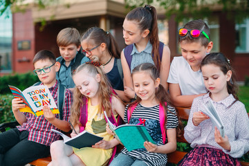 Happy Schoolmates Portrait. Schoolmates seating with books in a wooden bench in a city park and studying on sunny day.