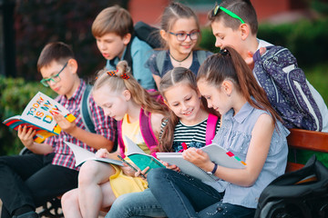Fototapeta na wymiar Happy Schoolmates Portrait. Schoolmates seating with books in a wooden bench in a city park and studying on sunny day.