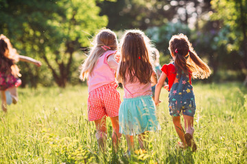 Large group of kids, friends boys and girls running in the park on sunny summer day in casual clothes .