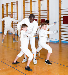 Focused boys fencers attentively listening to professional fencing coach in gym