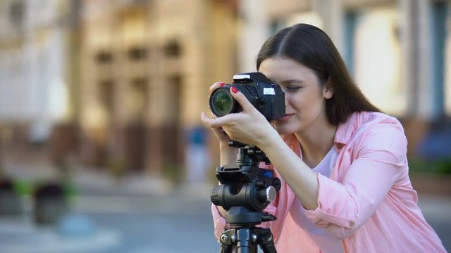 Smiling female photographer focusing camera objective on street, photo shooting
