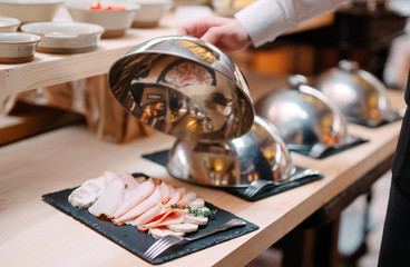 Meat slicing on a plate. The waiter holds the metal lid from the plate open.