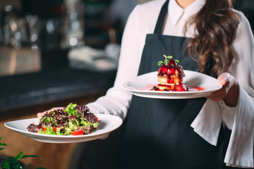 Waiter serving in motion on duty in restaurant. The waiter carries dishes