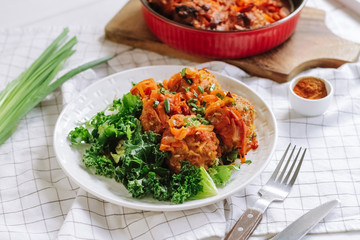 white bowl of home cooked meatballs with vegetables and salad leaves.