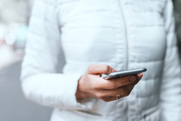 Close up of woman's hand holding grey smartphone and scrolling site on street.