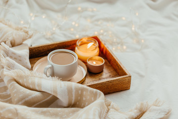 Tray of coffee and candles with warm plaid on white bedding . Breakfast in bed.  Scandinavian style.  Flat lay, top view