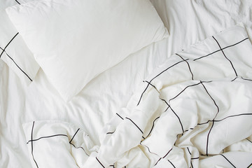 Fototapeta premium White bedding sheets with striped blanket and pillow. Messy bed. Cozy background.
