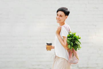 Young woman in light summer clothes with a eco bag of vegetables, greens and reusable coffee mug. Sustainable lifestyle. Eco friendly concept.