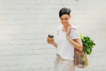 Young woman in light summer clothes with a eco bag of vegetables, greens and reusable coffee mug....