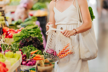 Young Woman puts fruits and vegetables in cotton produce bag at food market. Reusable eco bag for...