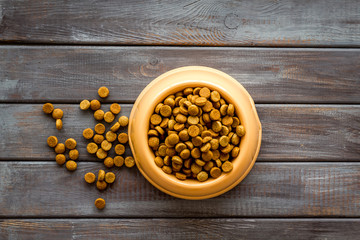 Dry pet food in bowls on wooden background top view