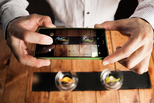 bartender shooting a picture with a cellphone to the glasses.