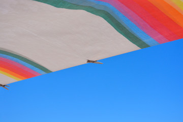 Rainbow coloured sheet hanging out to dry, blowing in the wind,  on washing line on sunny and very windy day. Selective focus on single wooden clothes peg.