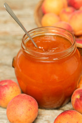 Jar of apricots jam and fresh apricots on wooden background