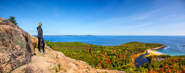 Female hiker standing on ledge enjoying view of water from Beehive Trail in Acadia National Park
