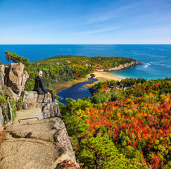 Female hiker sitting on ledge enjoying view of water from Beehive Trail in Acadia National Park - obrazy, fototapety, plakaty