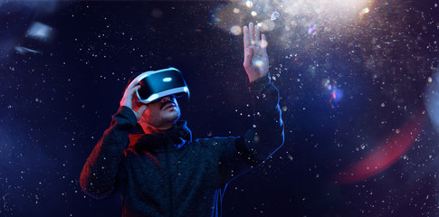 Young man over dark magic light background. Guy in glasses of virtual reality. Augmented reality,...