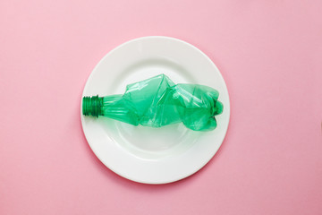 plastic pollution of food concept, white plate with clean crumpled green plastic bottle isolated on pink background