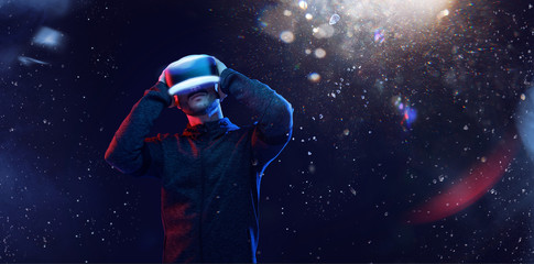 Young man over dark magic light background. Guy in glasses of virtual reality. Augmented reality, game, hobby concept. VR.