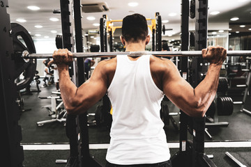 Man at the gym. Execute exercise squatting with weight, in gym