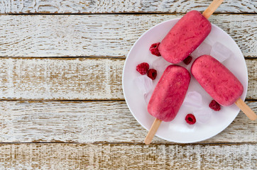 Strawberry and raspberry ice cream popsicles in white plate on white wooden background