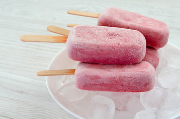 Strawberry and raspberry ice cream popsicles in white bowls on ice