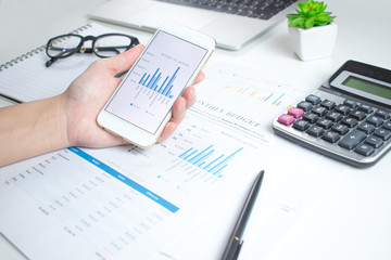 Businessmen use smartphones to calculate financial graphs on a white table.