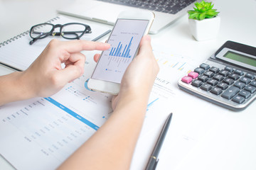 Close-up pictures of businessmen using smartphones. Calculate financial graphs on a white table.