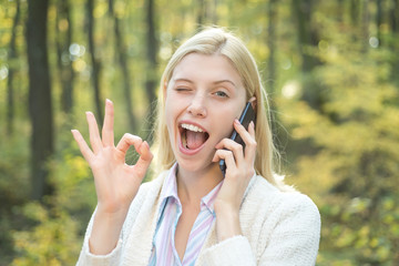 Happy girl posing winking with phone. Autumnal mood. Blonde woman rejoicing and holding mobile...