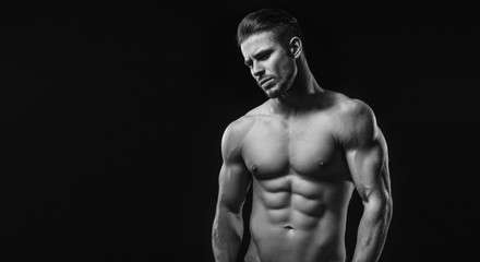 Black and white. Muscular model sports young man on dark background. Fashion portrait of strong brutal guy with a modern trendy hairstyle. Sexy torso. Male flexing his muscles.