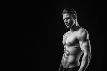 Fototapeta premium Black and white. Muscular model sports young man on dark background. Fashion portrait of strong brutal guy with a modern trendy hairstyle. Sexy torso. Male flexing his muscles.
