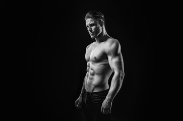 Fototapeta na wymiar Black and white. Muscular model sports young man on dark background. Fashion portrait of strong brutal guy with a modern trendy hairstyle. Sexy torso. Male flexing his muscles.