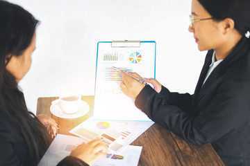 Asian business women working present the report graph financial information at the meeting in office the table desk - checking preparing sale report money analyzing graphs