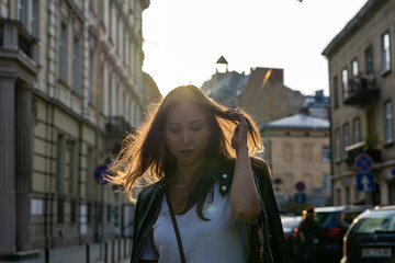 Beautiful girl is looking down. Street fashion photo shoot on a city street with backlight of sun on a hair