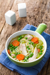 Fresh homemade chicken noodle soup with carrot, peas and celery in green soup bowl (Selective Focus, Focus in the middle of the soup)