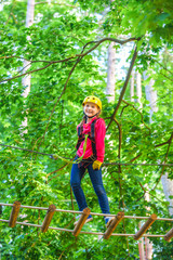 Naklejka na ściany i meble Beautiful little child climbing and having fun in adventure Park. Hiking in the rope park girl in safety equipment. Kid climbing trees in park. Cute child boy.