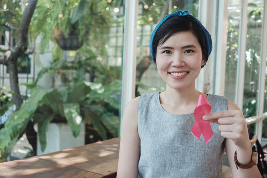 Asian woman holding pink ribbon, breast cancer awareness, October pink concept