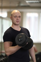 Fototapeta na wymiar european caucasian athletic man bodybuilder in black sportwear holding dumbell and showing his muscular arms. man doing exercise for biceps. Background is gym