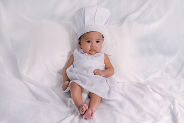 portrait of asian infant baby boy with white chef dress with white cloth background