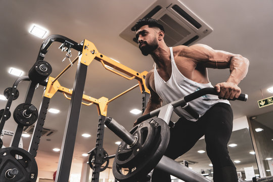 Muscular men exercising with weights. He is performing T bar rows for back muscle / Bodybuilder in the gym