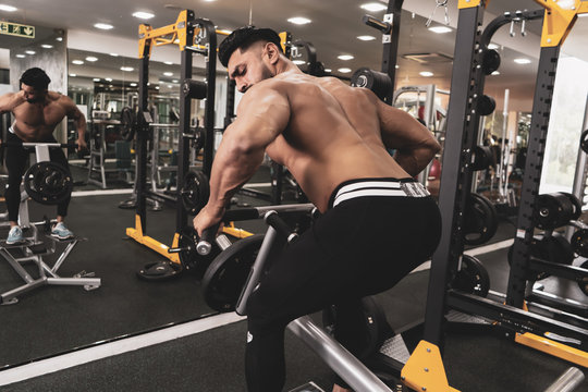 Muscular men exercising with weights. He is performing T bar rows for back muscle / Bodybuilder in the gym