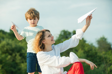 Mothers day. Happy mother and little son playing on blue summer sky. Happy family - mother and child on meadow with a toy paper airplane in the summer on the nature background.