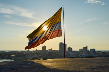 Warm Sunset behind Colombian flag in Castillo San Felipes de Barajas with the landscape view of the Cartagena`s city in the background (Cartagena - Colombia)
