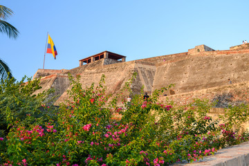 Side view of the Castillo de San Felipe de Barajas illuminated by the sunset, yellow tones, with a Colombian flag on the top (Cartagena - Colombia)