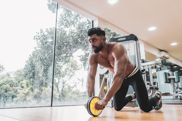 Athlete sporty man doing exercise with abs roller wheel to strengthen his abdominal muscle in gym. - obrazy, fototapety, plakaty