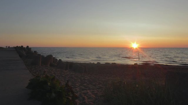 Time lapse of beautiful scenic beach view at sunset with silhouettes of people taking photos at the seaside near the Karosta North Pier, wide shot