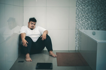 Unhappy fat man sits with a scale in the bathroom