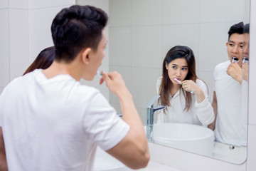 Fototapeta premium Young couple brushing teeth together in bathroom